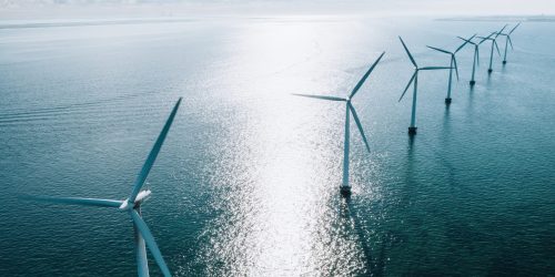 Offshore wind turbines in serene ocean, generating renewable energy under a bright blue sky.